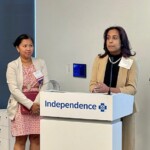 woman speaking at lectern with a young adult standing nearby